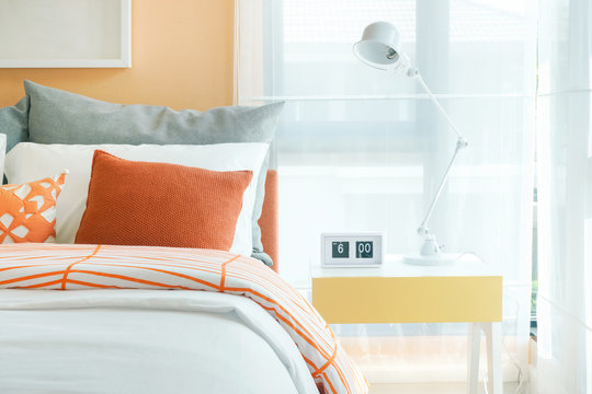 White foldable reading lamp on night table next to bed in orange and gray bedding style
