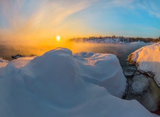 Winter dawn in the bay on the lake. Lake Ladoga in the cold. Open water hovers from frost. Granite skerries in the snow, in the ice.