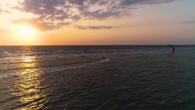 Drone flies after kiter, beautiful sunset in the sea. Sun among clouds