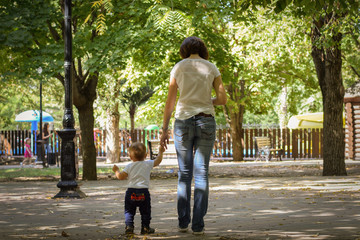 Mother walks with her child holding his hand in the autumn park. Responsible parenthood concept