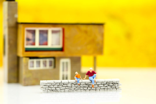 Miniature people : Family and children sitting of wall with house.