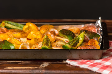 baking sheet, in the middle are vegetables, peppers, onions, potatoes and pieces of white meat sprinkled with spices and prepared for baking