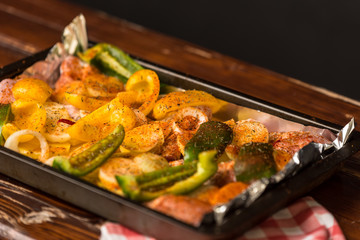 baking sheet, in the middle are vegetables, peppers, onions, potatoes and pieces of white meat sprinkled with spices and prepared for baking