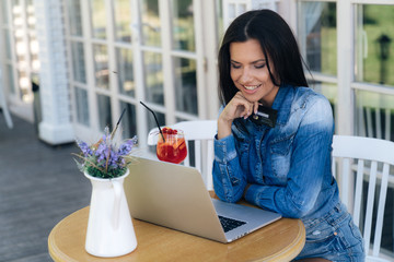 A happy radiant young woman uses a laptop for shopping on the Internet, holds a plastic card in her hand, wants to pay for her order.