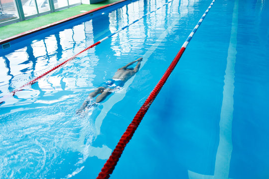 Photo on top of sports man in blue cap swimming on path in pool under water