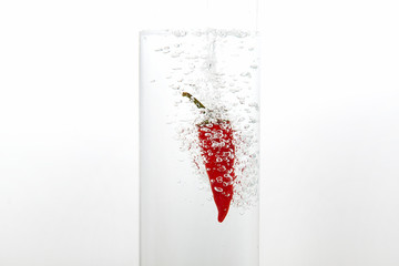 Red chilli pepper drops into clear clear water. There are a lot of bubbles in the water. White background, close-up