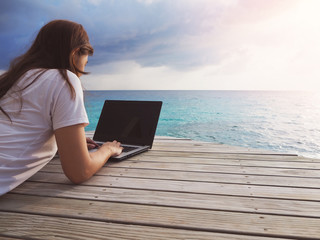 woman working with laptop sitting on wooden terrace in front of Beautiful turquoise sea in Maldives...