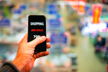 People, sale, consumerism, advertisement and black friday concept - close up of man's hand holding shopping bags and smartphone with shopping online inscription