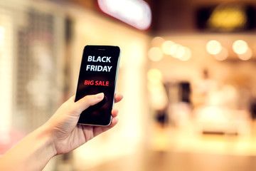 People, sale, consumerism, advertisement concept - close up of woman's hand holding shopping bags and smartphone with black friday inscription