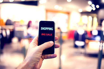 People, sale, consumerism, advertisement and black friday concept - close up of man's hand holding shopping bags and smartphone with shopping online inscription