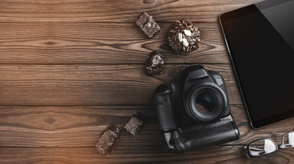 Camera photo, digital tablet, chocolate biscuits and eyeglasses on old wooden background. Top view,...