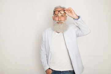 Cheerful happy mature man in glasses looking camera and smiling over white wall