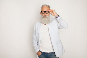 Cheerful happy mature man in glasses looking camera and smiling over white wall