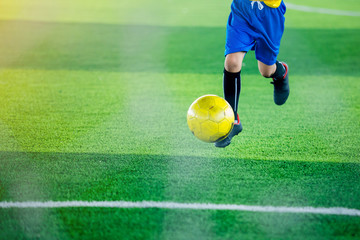 Kid soccer player shoot yellow ball on green artificial turf