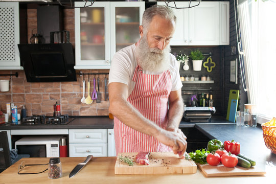 bearded senior man cooking steaks on his kitchen.