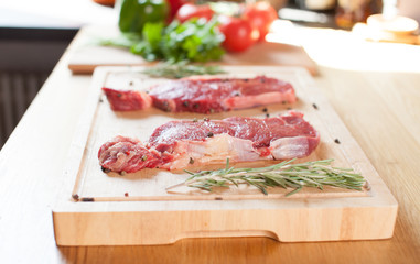 Raw beef tenderloin steak on a cutting board with rosemary pepper salt fork and cutter.