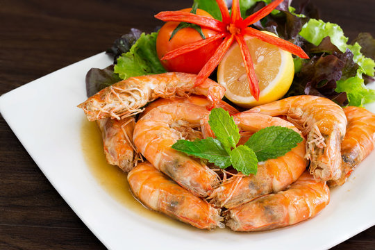 Bake shrimp with salt and sweet  in white dish which has fresh vegetables decorated on dish