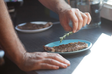 Close-up view man putting rosemary on grilled steaks