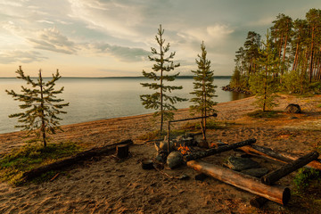 pines on the beach, bonfire, water as a mirror on the background of the setting sun