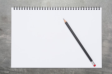 Blank page of a sketchbook with a black pencil on a grunge gray surface