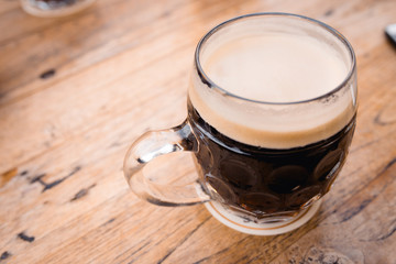 Close up top first person view photo of male holding brown black german ale czech natural glass beer cup on wooden brown tree old table. Photo in local rural pub bar Oktoberfest or event .  