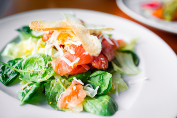 Closeup tasty grill vegetarian Slices of smoked salmon with bread, letuce arugula and cheese in european style, meal on large rounded white dish and spices on brown in urban modern stilysh restaurant