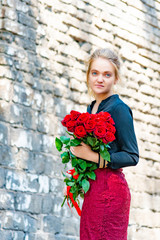 Beautiful and sexy girl with a bouquet of red roses stands on the background of an old brick wall.