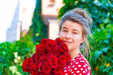 Beautiful and sexy girl with a bouquet of red roses stands on the background of an old brick wall.