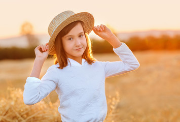 Beautiful girl in a straw hat sits on a haystack at sunset in the evening