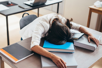 Tired female student sleeping on desk face and hands on books