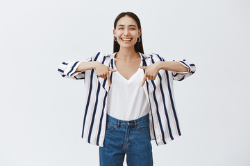 Indoor shot of amazed carefree beautiful woman in striped blouse and jeans, laughing out loud from...