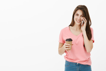 Portrait of joyfull good-looking girlfriend in trendy urban outfit talking on smartphone casually and smiling broadly at camera while talking with friend and drinking coffee, walking to office