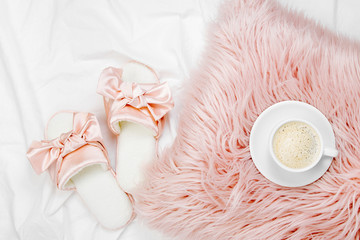 Morning concept. A cup of coffee on a pink pillow, slippers on the bed. Flat lay, top view