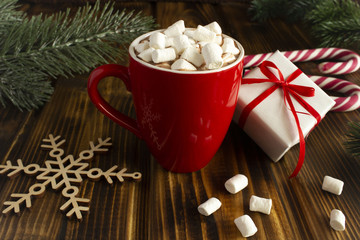 Obraz na płótnie Canvas Hot chocolate with marshmallows, Christmas gift and candy canes on the brown wooden background.