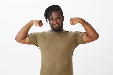 Portrait of serious-looking masculine dark-skinned plump guy in military clothes, raising hands and...