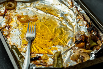 used baking tray, silver foil, roasting remnants, fat and dirty fork on it