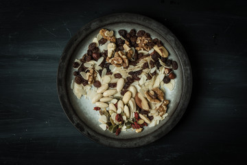 view form the top, on a black, rustic, wooden table stands a white plate with hand-painted black edges full of various nuts