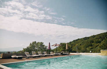 Swimming pool with sunbeds and sun umbrella and mountains in the background.