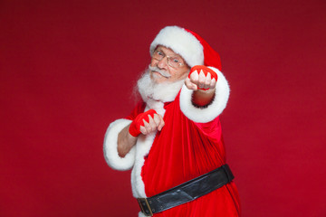Christmas. Santa Claus with red bandages wound on his hands for boxing imitates kicks. Kickboxing, karate, boxing. Isolated on red background.