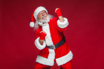 Christmas. Santa Claus with red bandages wound on his hands for boxing imitates kicks. Kickboxing, karate, boxing. Isolated on red background.