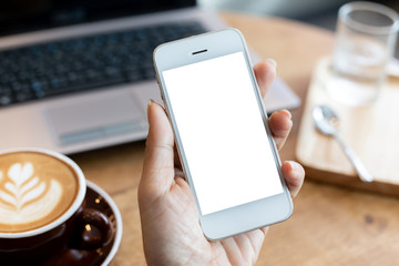 hand woman using a telephone, empty screen smart phone and computer on wooden table In the coffee shop. with clipping path
