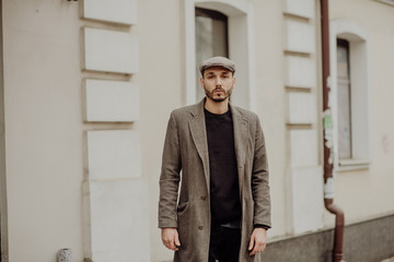 City life. Filtered effect. Stylish young American man standing on the street. Businessman wearing a grey fashionable trench coat and hat.