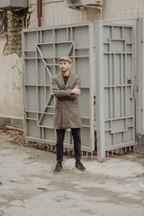 City life. Filtered effect. Stylish young American man standing on the street. Businessman wearing a grey fashionable trench coat and hat.