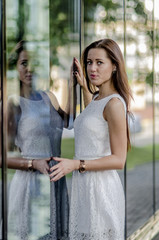 Obraz premium Beautiful young girl in a white summer dress near a showcase with reflection 