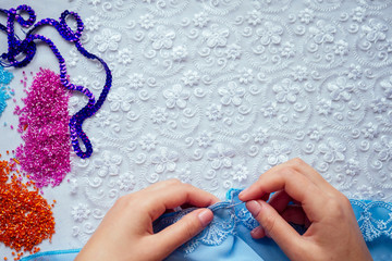 close-up hands of woman seamstress tailor ( dressmaker) designer wedding dress sews beads to lace on a blue background in the studio