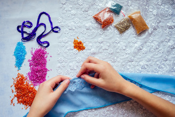 Obraz na płótnie Canvas close-up hands of woman seamstress tailor ( dressmaker) designer wedding dress sews beads to lace on a blue background in the studio