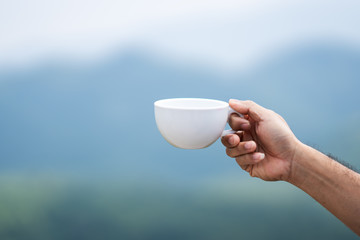 Coffee cup on hand holding on blurred beautiful mountain and sky