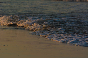 Dark blue sea waves closeup with white foam on a sand beach at the sunset