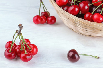 Composition with ripe cherries close-up and basket with cherries in the background on a white wooden table