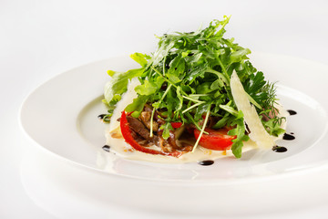 Plate of beef salad served with parmesan, green and tomato isolated at white background.